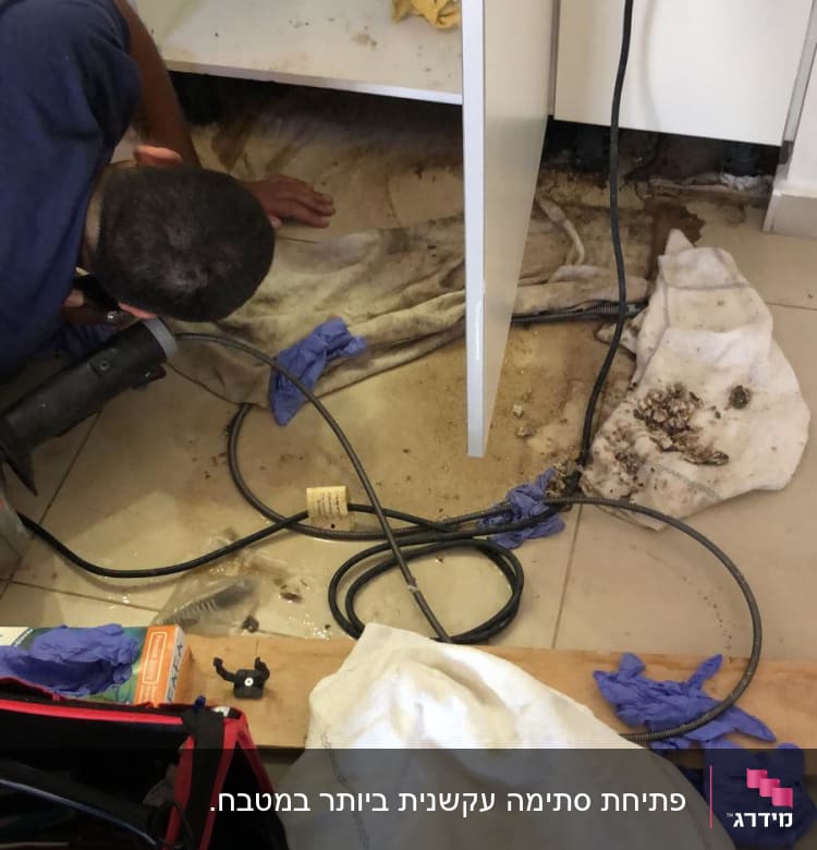 אדם עובד מתחת לכיור עם כלים וצינורות